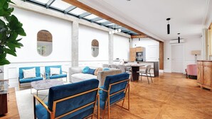 A spacious living area with a high ceiling, wooden beams, and a large window. - A PERFECT BLEND OF CLASSIC ELEGANCE & MODERN COMFORT NEXT TO LUXEMBOURG GARDEN (Paris)