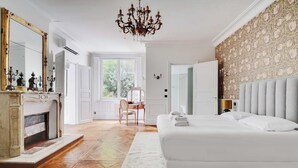 A spacious bedroom with a large bed, a fireplace, a chandelier, and a view of the outdoors. - A PERFECT BLEND OF CLASSIC ELEGANCE & MODERN COMFORT NEXT TO LUXEMBOURG GARDEN (Paris)