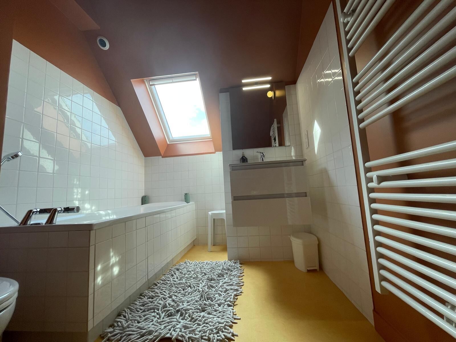 Een moderne badkamer met dakraam, witte tegels, een badkuip, toilet en radiator.