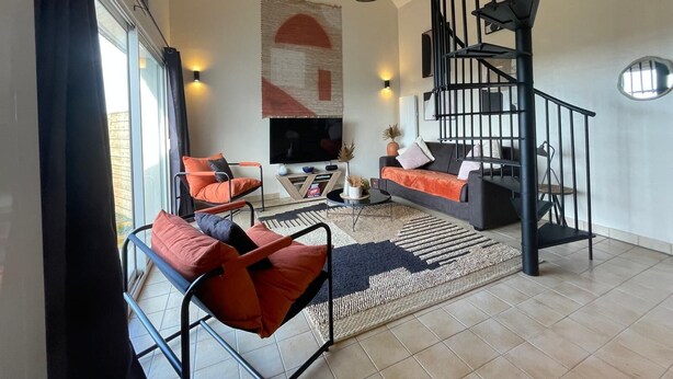 A modern living room with a black spiral staircase, a large TV, and orange and black furniture.