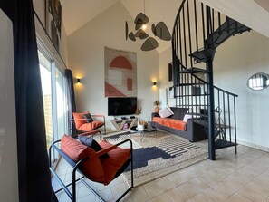 Una sala de estar moderna con una escalera espiral negra, un televisor grande y mobiliario naranja y negro.