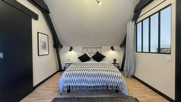Une chambre moderne avec un grand lit, un luminaire au plafond, un tableau encadré au mur et une fenêtre sur le côté droit.