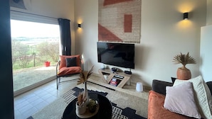 A modern living room with a large TV, comfortable seating, a coffee table, and a view of the outdoors.