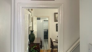 Un couloir mène à une salle à manger où se trouvent une table, des chaises et un vase vert.