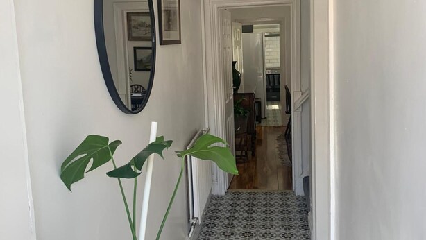 Un couloir avec un miroir, des tableaux encadrés et un escalier menant à une pièce.