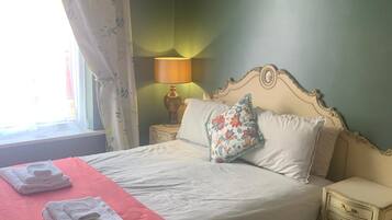 A neatly made bed with a pink bedspread, a floral pillow, and folded towels on the side.