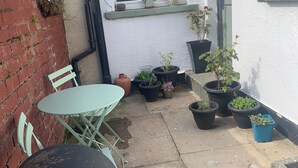 Un petit espace patio avec une table ronde et des chaises, entouré de plantes en pot et d’un mur de briques.