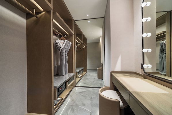 Un baño moderno con tocador, espejo con iluminación y un vestidor con batas colgadas.