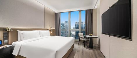 A hotel room with a large bed, a desk with a chair, a flat-screen TV, and a view of the cityscape.