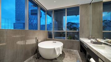 A modern bathroom with a freestanding bathtub, a large mirror, and a view of a cityscape through large windows.