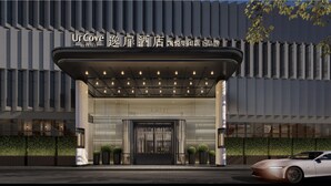 L’entrée moderne d’un hôtel, avec un auvent illuminé, de grandes fenêtres et une voiture garée devant.
