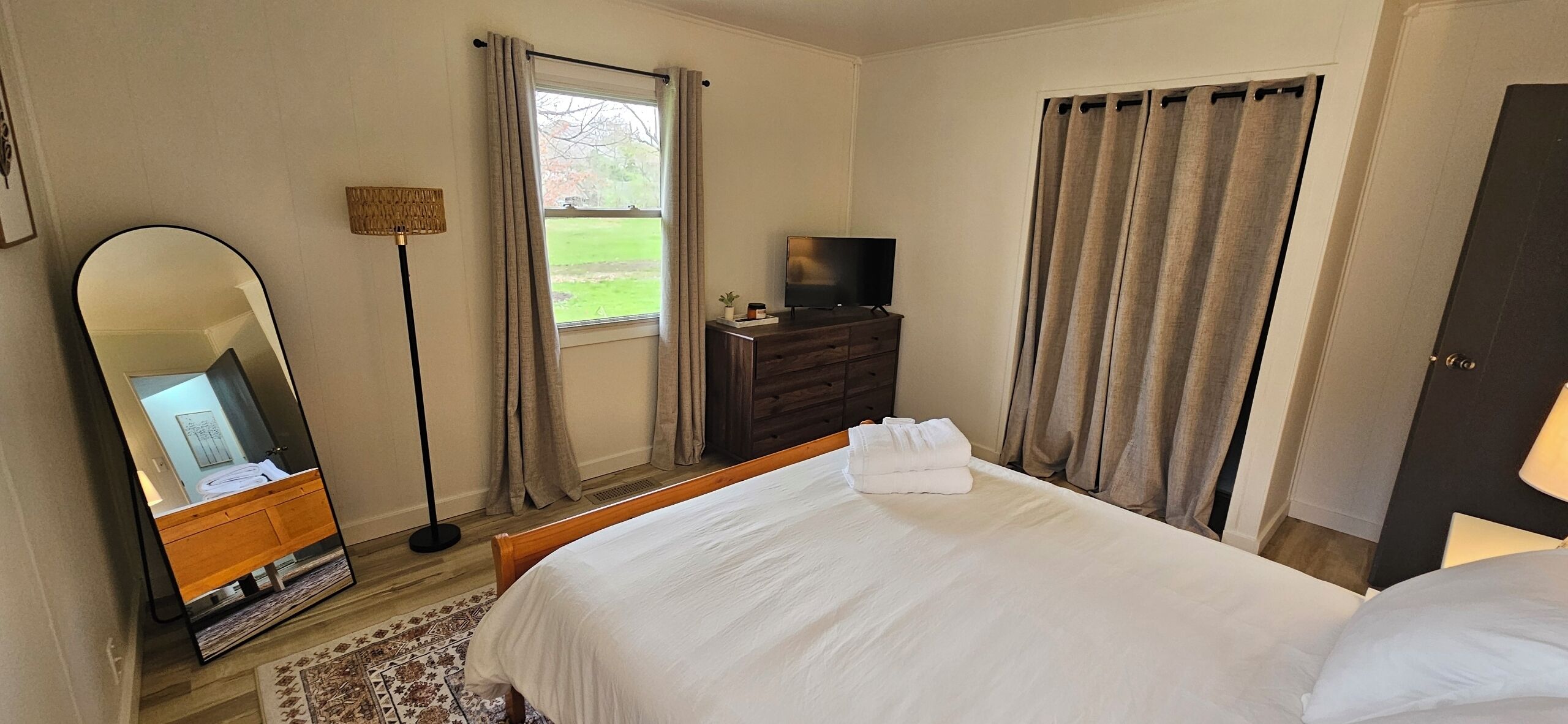 Una habitación de hotel con cama, cómoda, televisor y ventana con cortinas.