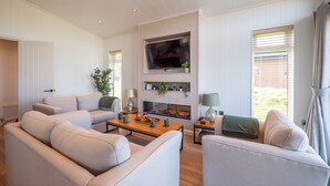 A living room with a sofa, coffee table, and TV. There is a fireplace with plants on shelves above it. - Countryside Lodge Retreat on Golf Course (Blackawton)