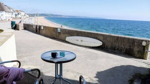 A balcony with a table and chairs overlooking a beach and the sea. - ​Beachfront Cottage with Sea Views & Coastal Walks​ (Torcross)