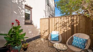 A patio with a wooden fence, a potted plant, and two wicker chairs with cushions.