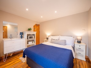 Quarto com cama, mesas de cabeceira, cômoda, espelho, micro-ondas e guarda-roupa de madeira.