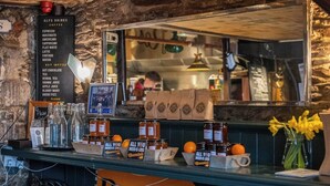 A coffee shop counter with a menu listing coffee and hot drinks, jars of marmalade, and a mirror reflecting the interior.