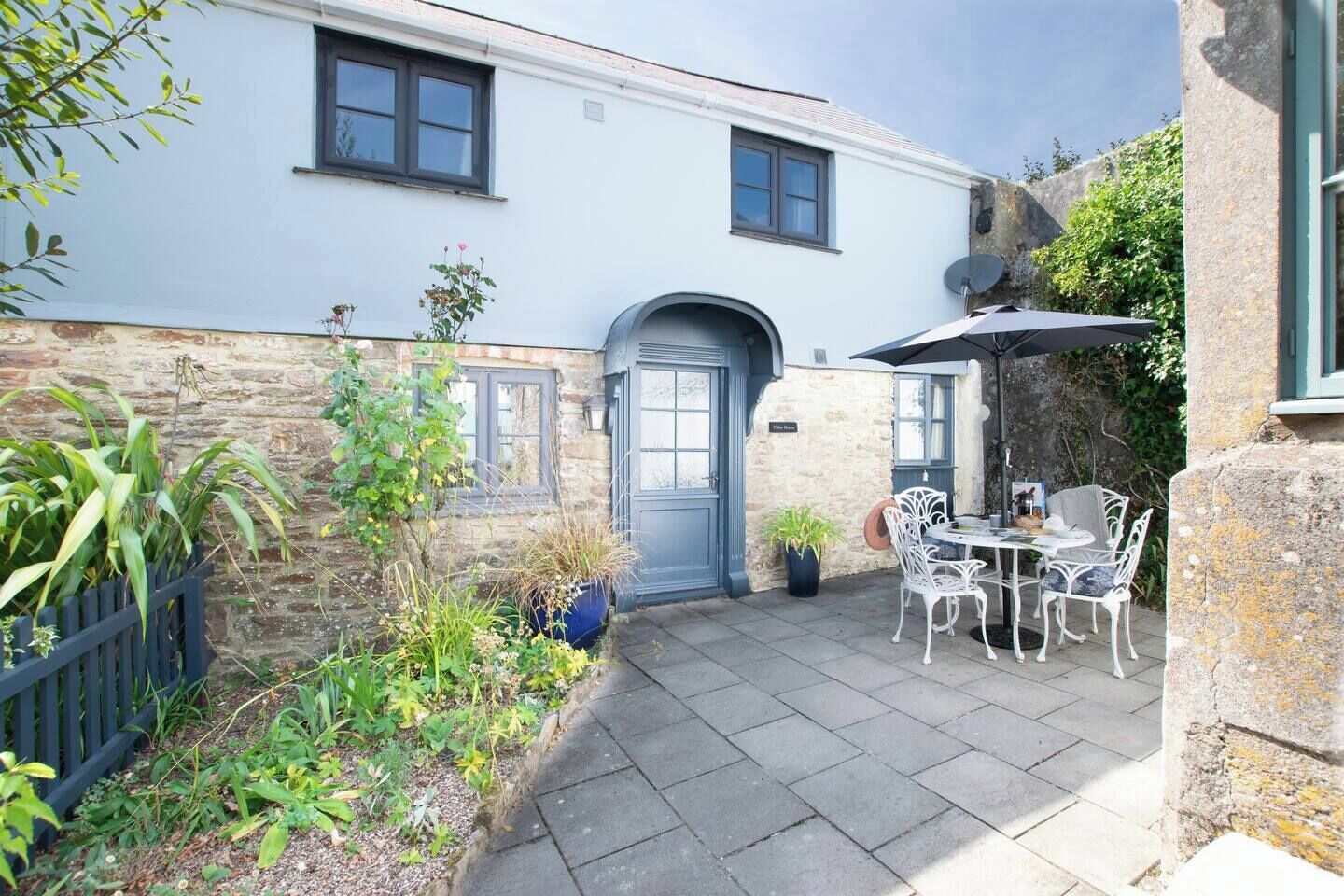 A courtyard with a blue door, stone wall, potted plants, and outdoor seating.