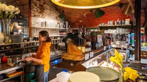 A bar with a rustic interior, shelves with bottles and glasses, and a person working at the bar. - B&B Bunk Room Above Café Alf Resco in Dartmouth (Dartmouth)