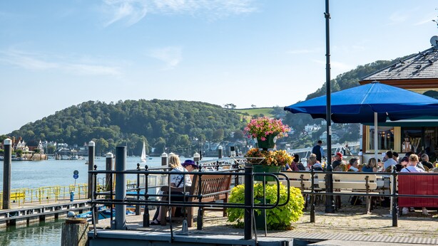 A waterfront restaurant with outdoor seating, a dock with boats, and a hill in the background. - B&B Bunk Room Above Café Alf Resco in Dartmouth (Dartmouth)