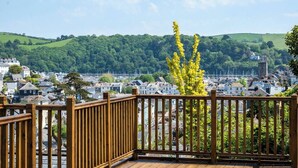 Une terrasse en bois offrant une vue sur une ville côtière, avec des maisons, une église et une colline verdoyante.