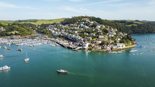 Une ville côtière dotée d’un port de plaisance rempli de bateaux, entourée de collines verdoyantes et d’une colline plus imposante sur laquelle se dressent des bâtiments.