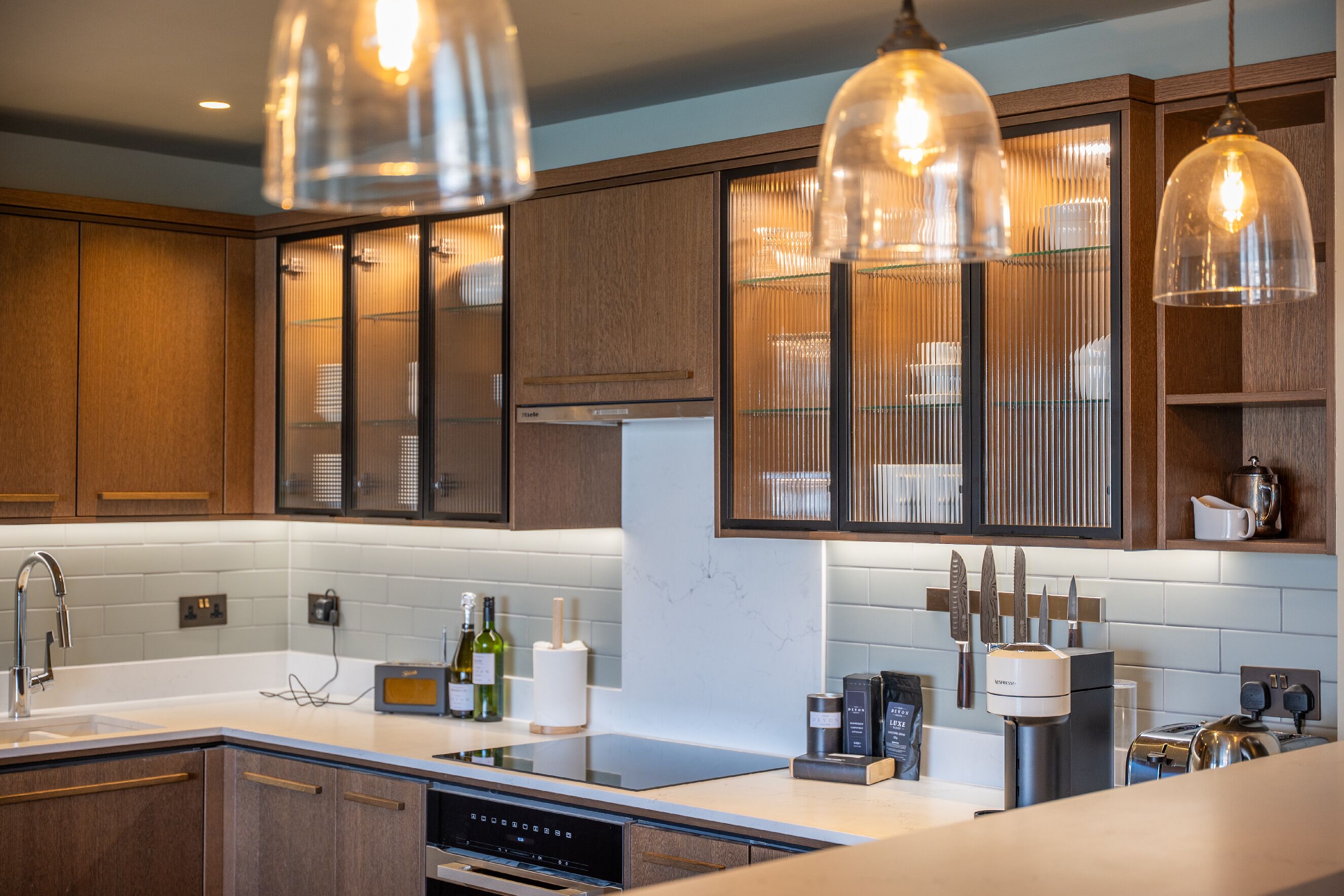 A modern kitchen with wooden cabinets, a built-in oven, a sink, and a coffee maker.
