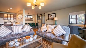 A cozy living room with two sofas, a coffee table with breakfast items, a dining area with chairs, and a kitchen in the background. - Stylish Waterfront Home With River Dart Views (Dartmouth)