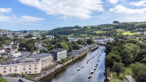 A riverside town with a canal lined with boats, buildings, and greenery.
