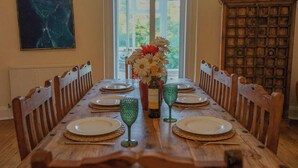 A dining table set for six with a vase of flowers, wine bottle, and green wine glasses.