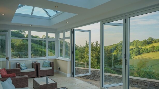 A spacious sunroom with large glass doors and windows, wicker furniture, and a view of a green landscape.