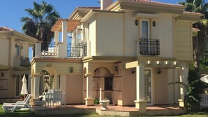 Uma casa de dois andares com varanda, um pátio com mobiliário exterior e um gramado bem cuidado.