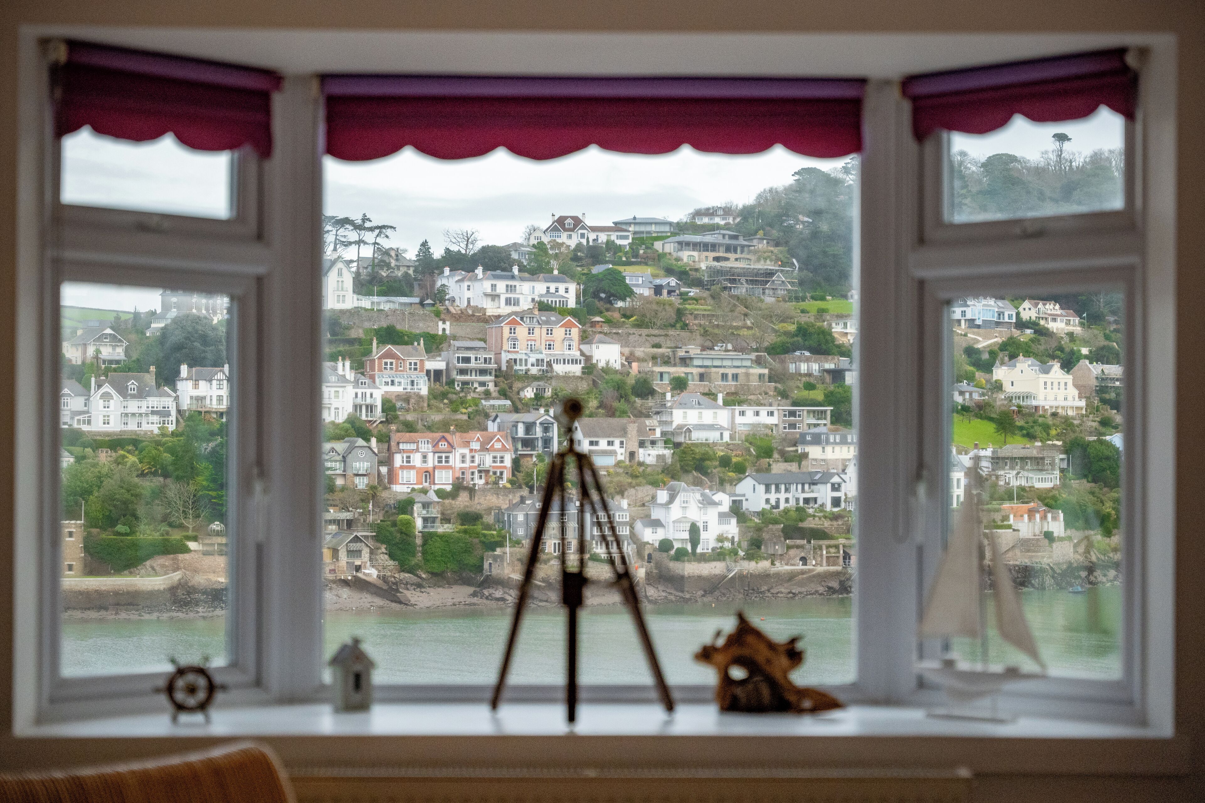 A room with a large window overlooking a hillside with houses.