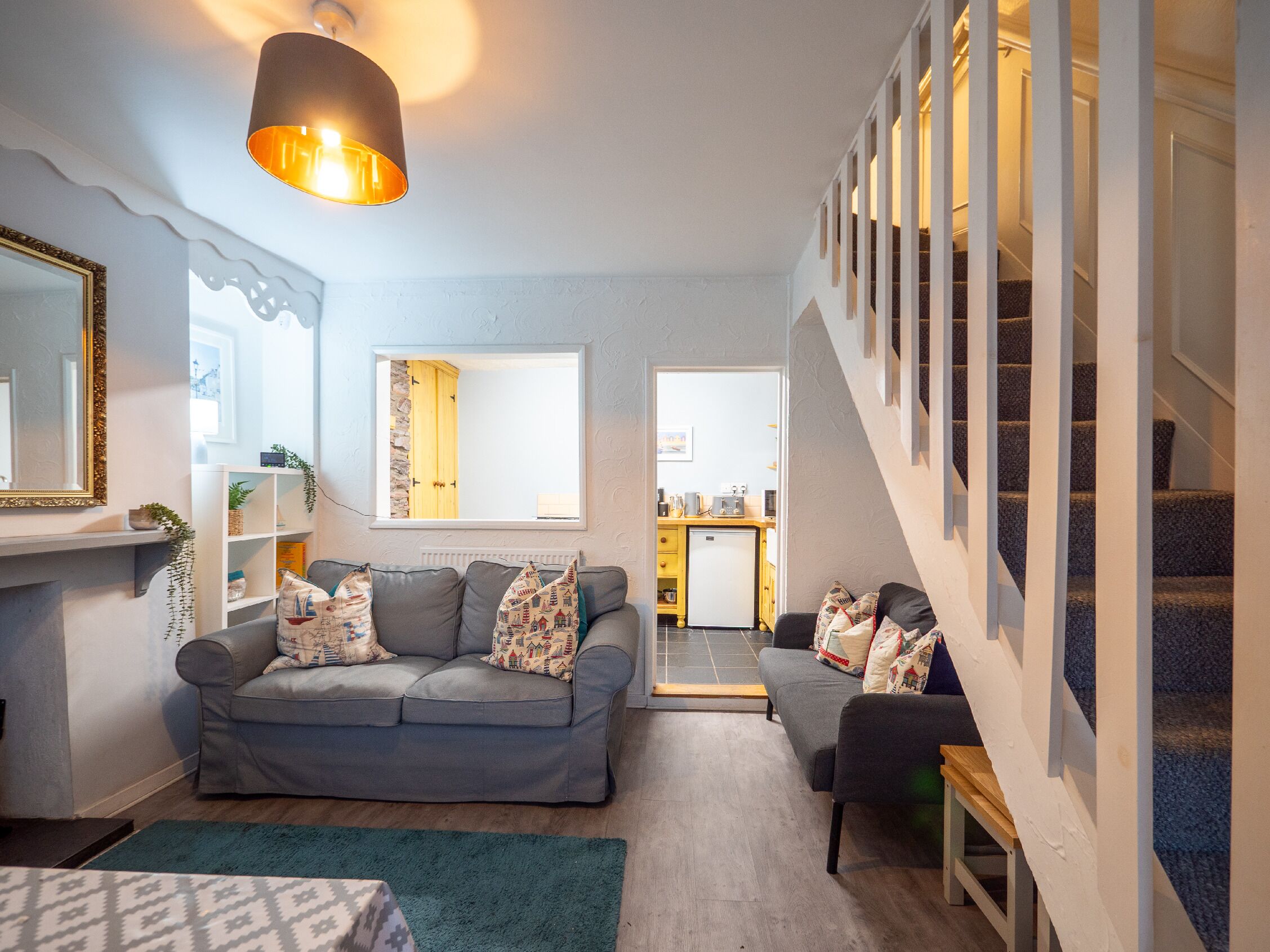 En moderne stue med en grå sofa, et lille bord og en trappe, der fører til et øvre plan.