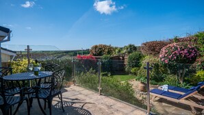 Eine Terrasse mit Tisch und Stühlen, ein kleiner Garten mit Blumen und eine Aussicht auf die Landschaft.