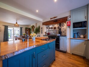 A kitchen with blue cabinets, a wooden countertop, and a hanging pot rack. - Farmhouse with Garden & Countryside Views (Totnes)