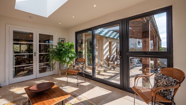 A spacious room with a large skylight, a dining area with a wooden table and chairs, and a view of the outside through large windows. - Farmhouse with Garden & Countryside Views (Totnes)
