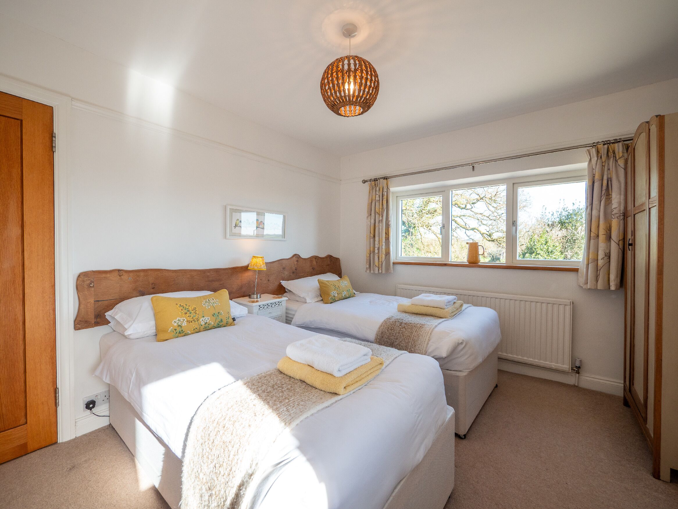 A bedroom with two beds, a window with curtains, a lamp, and a radiator.