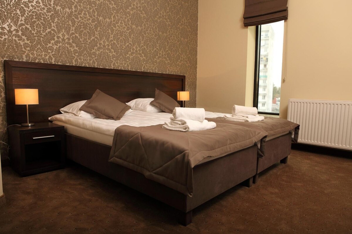 A neatly made bed with pillows and a blanket, a bedside lamp, and a window with a view.