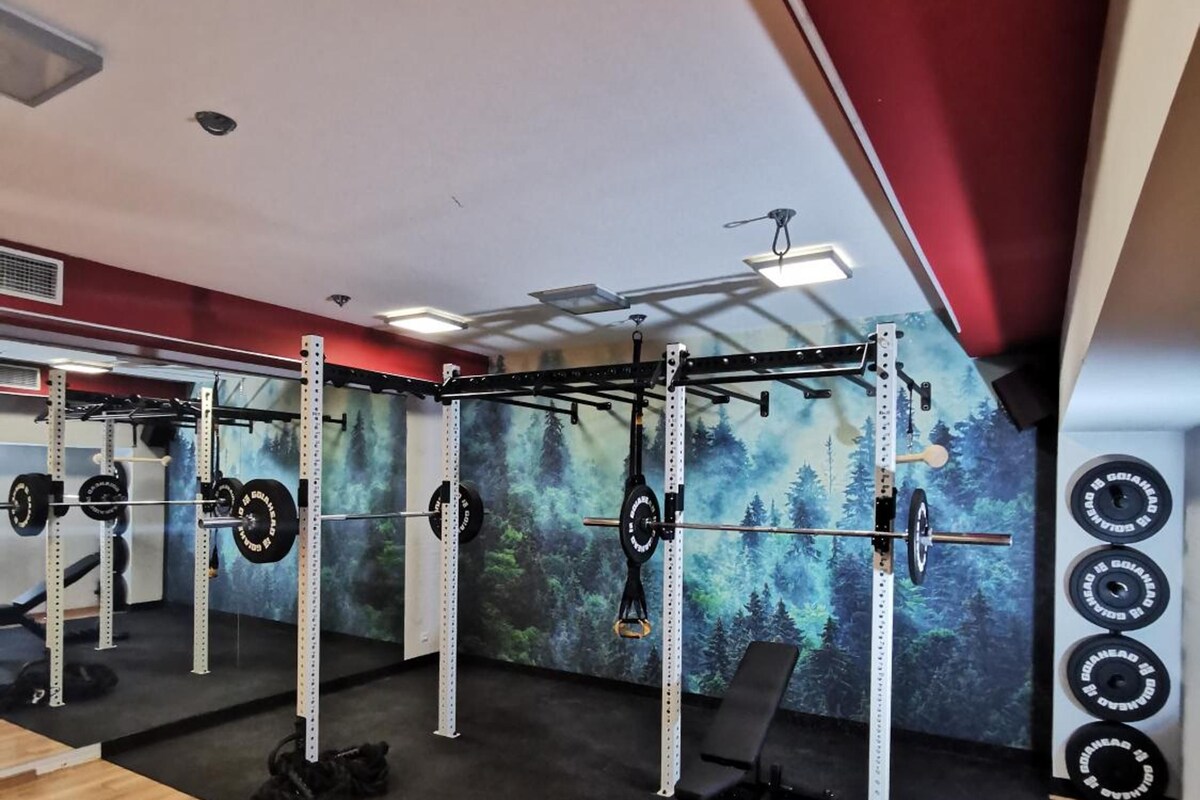 A gym with weightlifting equipment, a bench, and a wall with a forest mural.