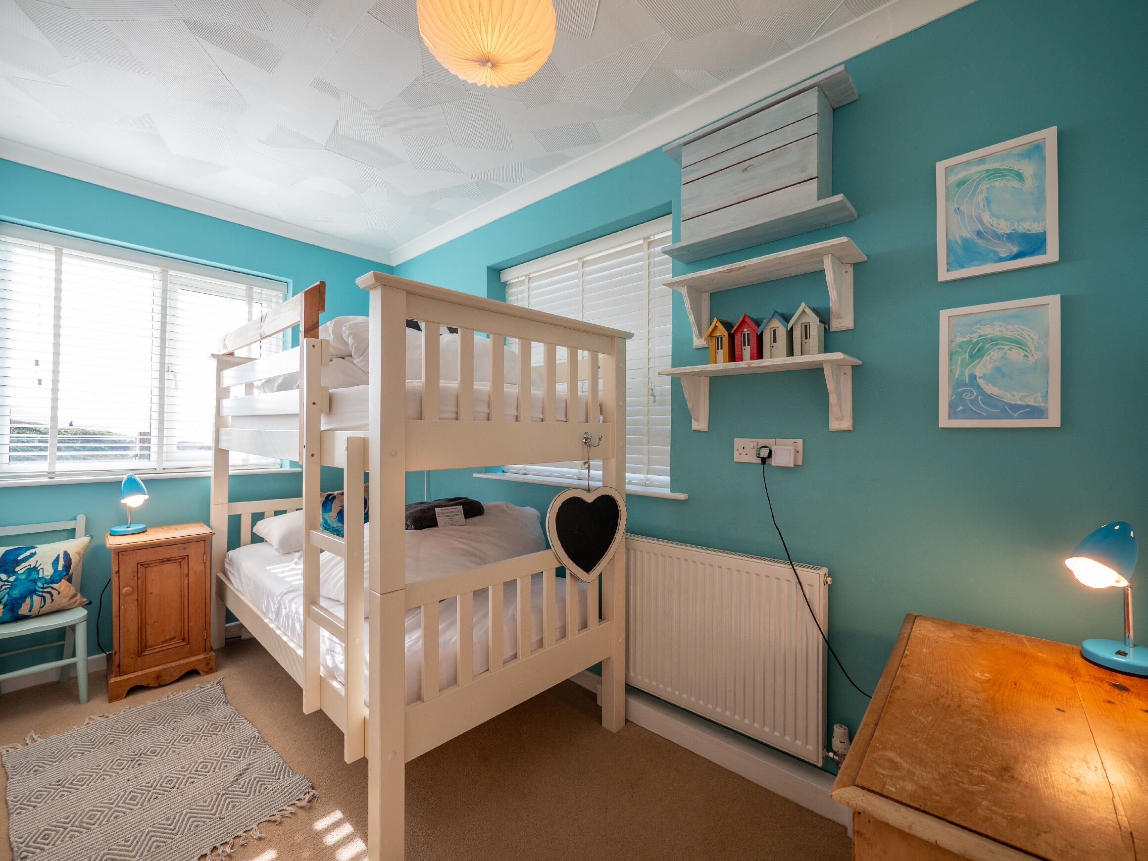 A bunk bed with a heart-shaped decoration, a wooden cabinet, a radiator, and a shelf with small houses.