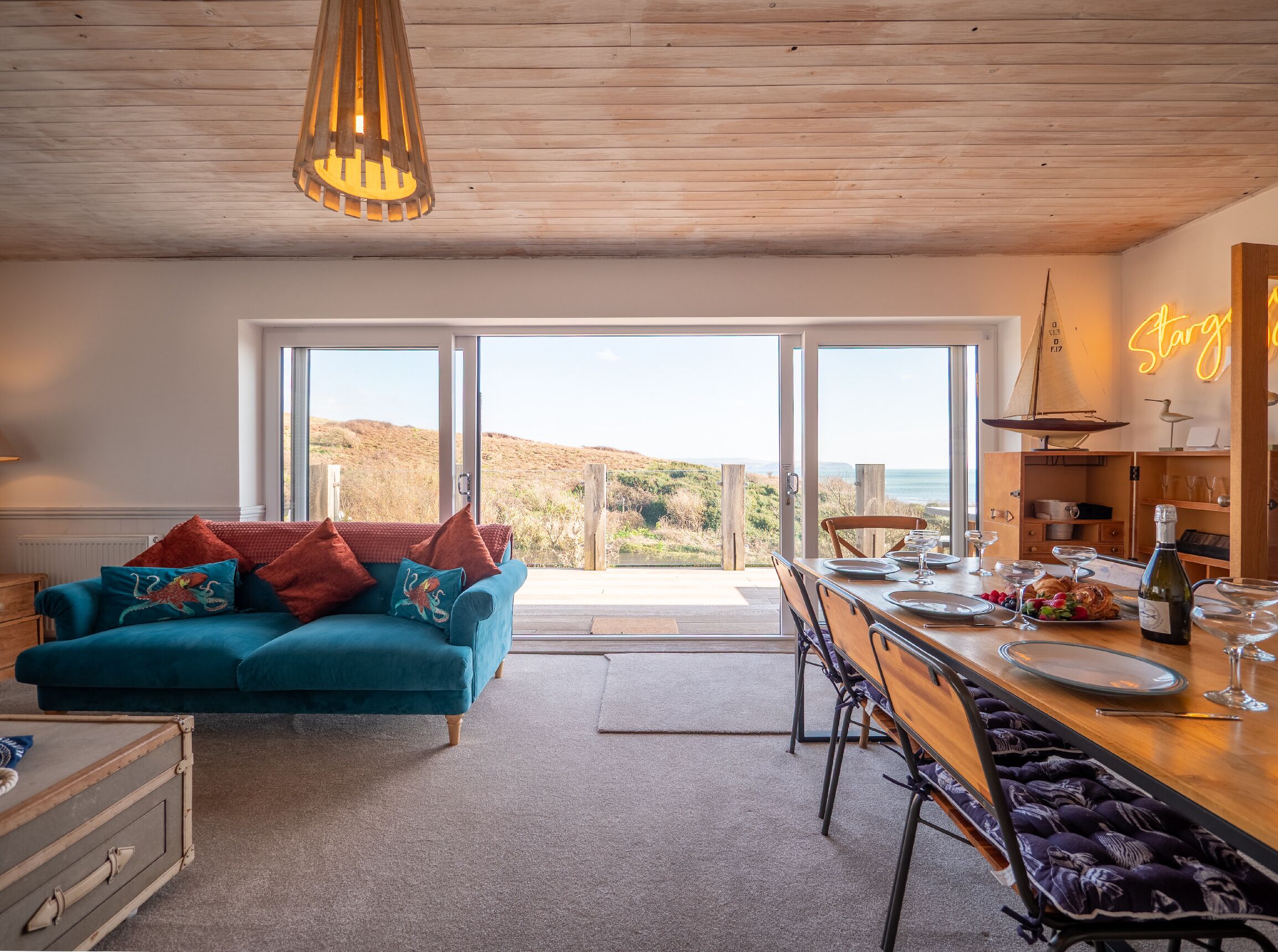 Un salon chaleureux avec un canapé de couleur turquoise, une table à manger en bois et une vue sur les collines.