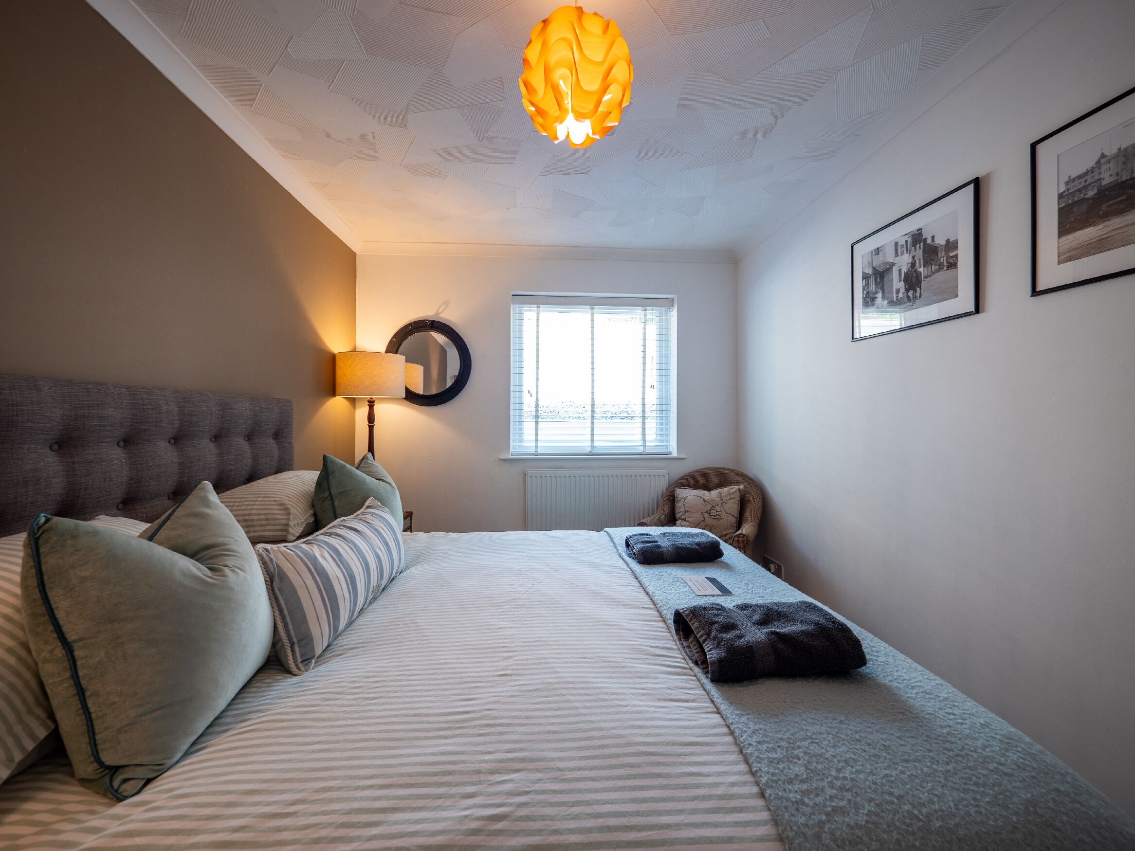 Una camera da letto con un letto, una lampada da comodino, una finestra e quadri appesi al muro.