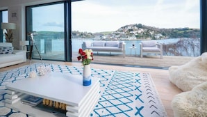 Ein modernes Wohnzimmer mit einem großen Glasfenster, das auf einen Balkon mit Blick auf eine Küstenstadt führt.