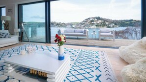 A modern living room with a large glass door leading to a balcony overlooking a coastal town.