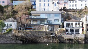 A coastal building with a stone retaining wall, a balcony, and a view of the sea.