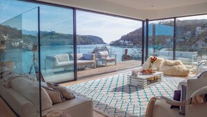 A modern living room with a large glass wall offering a scenic view of a lake and hills.