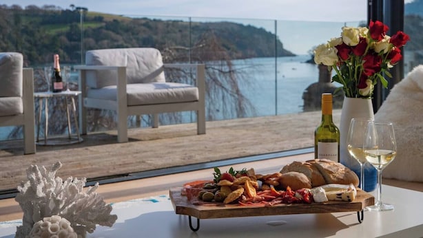 A dining table with a charcuterie board, wine glasses, and a bottle of wine, overlooking a scenic coastal view.