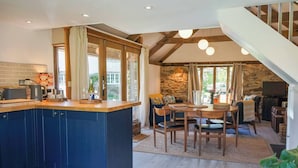 A modern kitchen with a central island, a dining area with a wooden table and chairs, and a stone wall in the background. - Escape to an Idyllic Countryside Couple's Retreat (Totnes)