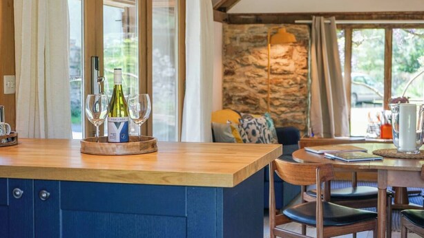 A kitchen with a wooden countertop, wine bottles, and glasses. There is a stone wall and a dining area with a table and chairs. - Escape to an Idyllic Countryside Couple's Retreat (Totnes)